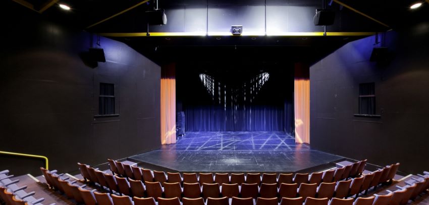 Empty theatre with stage, blue-lit curtains, and tiered seating