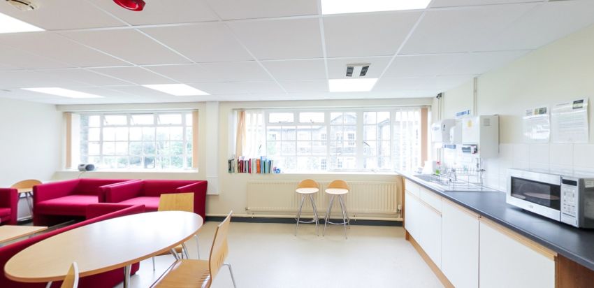 Common room with seating area, tables and kitchenette by large windows