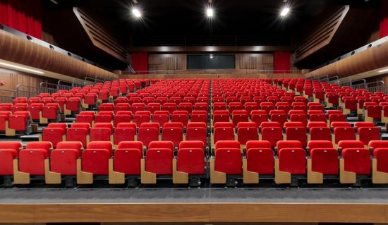 Empty auditorium with rows of red seats facing a stage in a modern hall