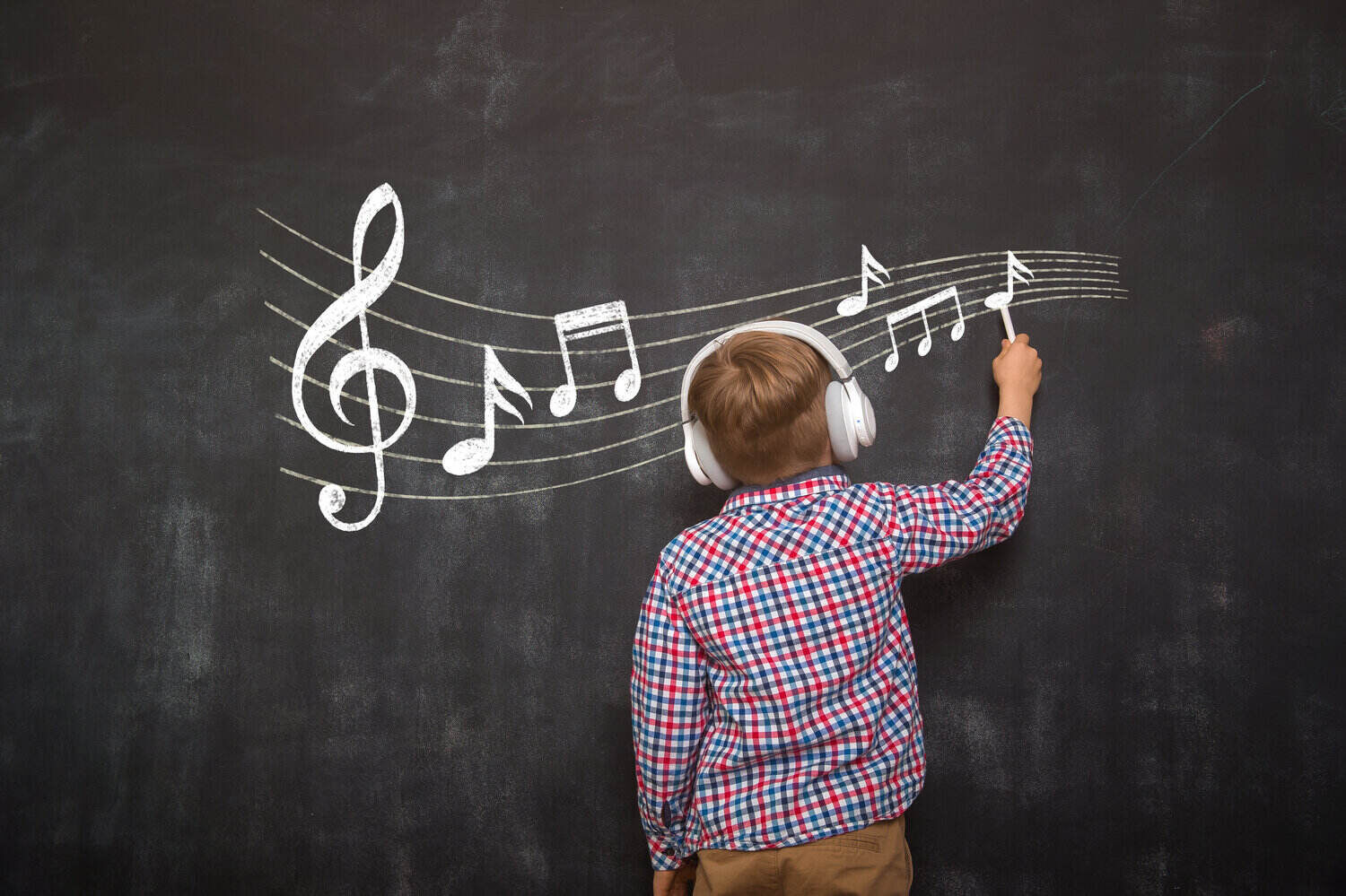 Boy with headphones on drawing music notes on a blackboard